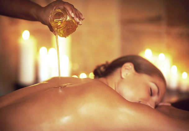 Where stress ends and relaxation begins.... Shot of a masseuse pouring oil on a womans back before her massage. - Photo, Image