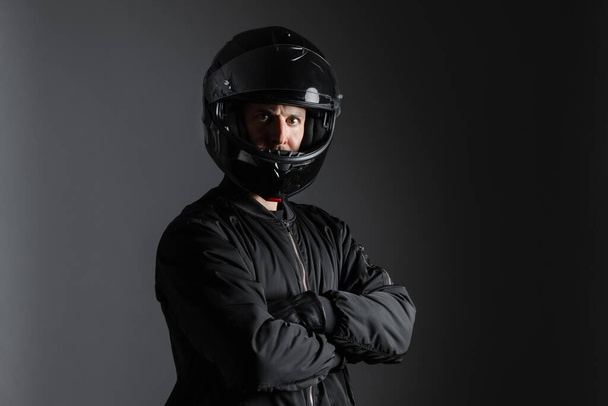 Studio shot of Motorcyclist biker in black equipment with crossed arms. - Фото, изображение