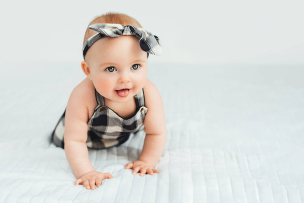 Cute smiling little baby girl sitting on bed. Seven month old infant child on grey soft blanket - Photo, image