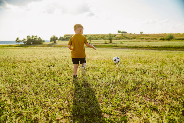 Blonde little white boy running across field and playing football outdoors - Photo, Image