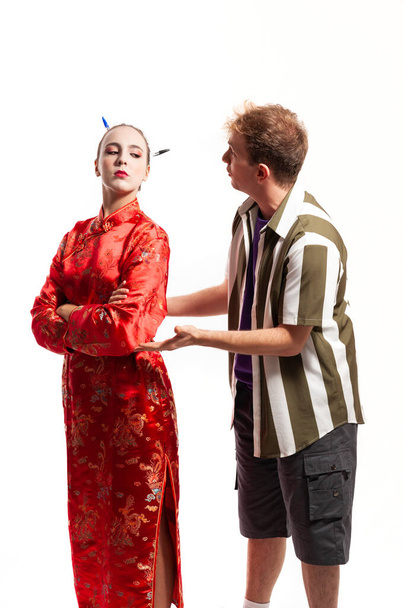 многонациональная пара, мужчина и женщина. Женщина, одетая в традиционный красный китайский костюм, смотрит через плечо, а мужчина, одетый в рубашку, просит и объясняет:. - Фото, изображение