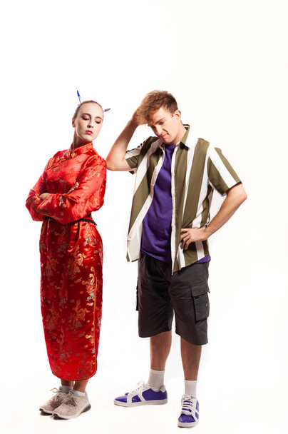 multiethnisches Paar, männlich und weiblich. Frau in traditionellem chinesischem roten Kleid blickt über ihre Schulter und Mann im Hemd denkt, er kratzt sich am Kopf. - Foto, Bild
