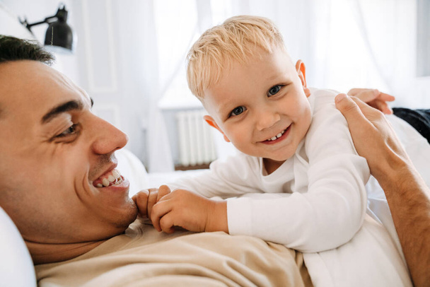 Young white father making fun and playing with his son on bed at home - Foto, Imagen