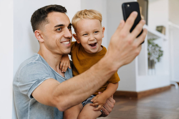 Young father and son smiling and taking selfie photo on mobile phone at home - Foto, immagini