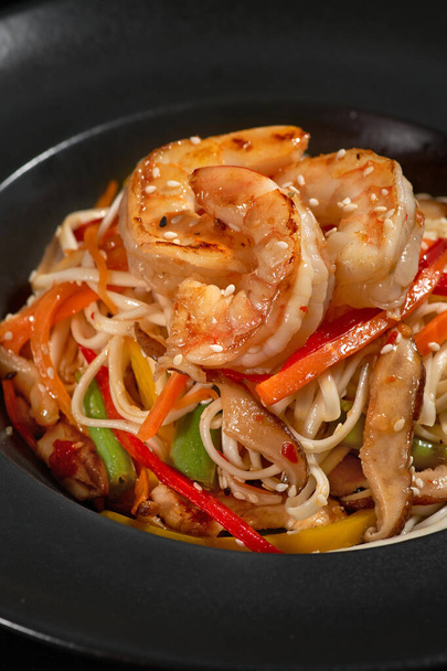 Traditional Asian Pasta. udon noodles with shrimp and vegetables on a plate on black stone background. Wok menu. Vertical top view from above - Foto, afbeelding