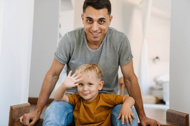 Young white father smiling while sitting with his son on stairs at home - Foto, Imagem