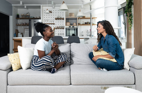 Two best friends hanging out at home together and having fun while sitting on the couch in cozy modern apartment. Two women gossip about the men they met last night out at the party in the club. - Photo, Image