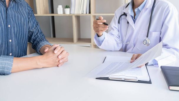 Patient hört aufmerksam zu, wie ein männlicher Arzt die Symptome des Patienten erklärt oder eine Frage stellt, während sie in einer Konsultation gemeinsam den Papierkram besprechen - Foto, Bild
