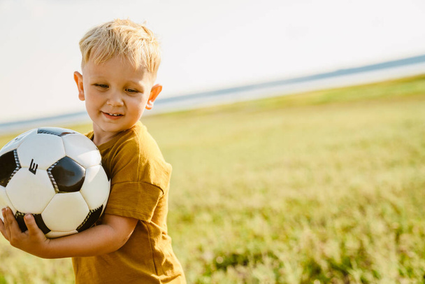 Blonde white boy smiling while playing football outdoors - Fotó, kép