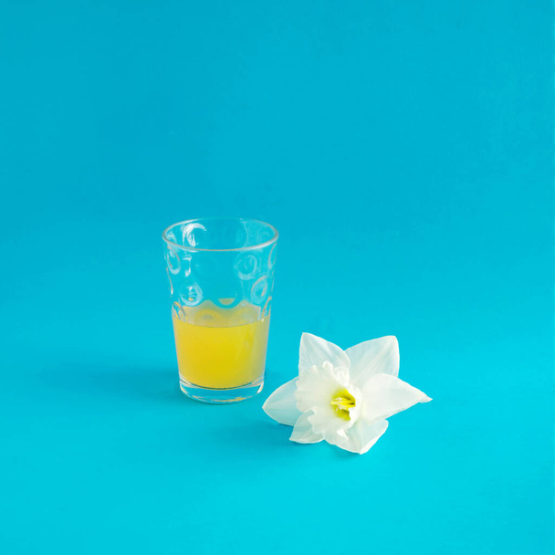 Ένα ποτήρι χυμό που σερβίρεται με λευκά λουλούδια νάρκισσος σε μπλε φόντο - Φωτογραφία, εικόνα