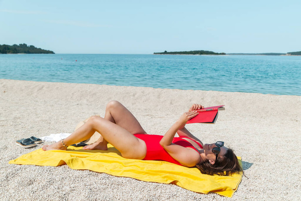 giovane donna sexy mozzafiato in costume da bagno rosso libro di lettura sulla spiaggia del mare. Ora legale - Foto, immagini