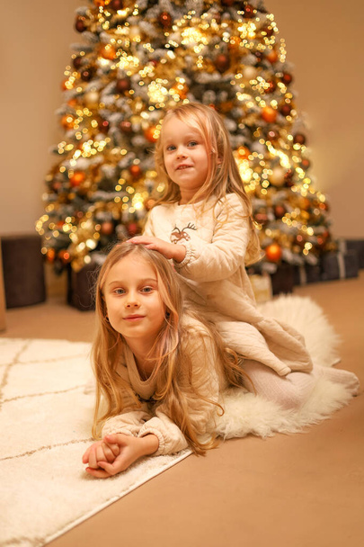 Christmas holiday, happy sisters, girls near the Christmas tree - Фото, изображение