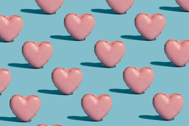 Pattern created of artisan french patisserie concept. Pink heart shaped yummy irresistible macaron alone against baby blue background - Фото, зображення