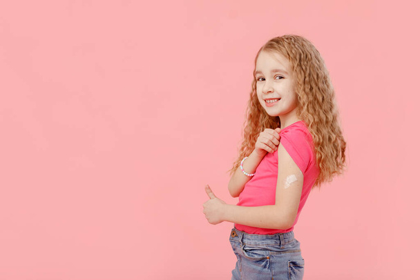 Vakcinační koncept. roztomilá holčička, předškolačka, s náplastí na rameni, dostala vakcínu, ochranu proti covid 19, a další nemoci, stojí na izolovaném růžovém pozadí, usmívá. - Fotografie, Obrázek