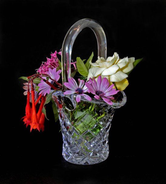 Kevert, színes, friss virágok gyűjteménye egy gyönyörű vágott üvegkosár vázában, fekete színű háttérrel elszigetelve. Fali művészet és dekoráció kép. - Fotó, kép
