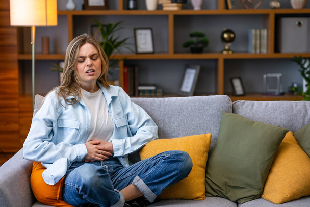 Young woman frowning having stomach ache sitting on the couch - Fotoğraf, Görsel