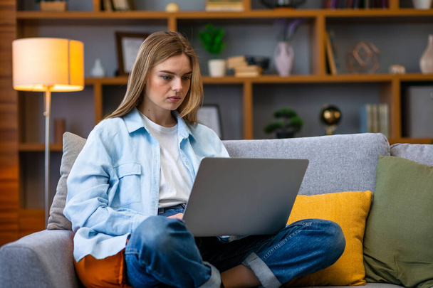 Serious woman sitting on sofa relaxing while browsing online shopping website. Happy girl browsing through the internet during free time at home. - Foto, Imagem