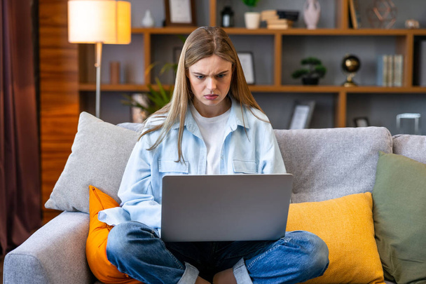 Wściekła młoda kobieta siedzieć na kanapie w salonie mając problemy operacyjne laptopa, irytowany powolnym połączeniem internetowym, mylić dziewczyna pracuje z domu doświadczenie system awarii oprogramowania - Zdjęcie, obraz