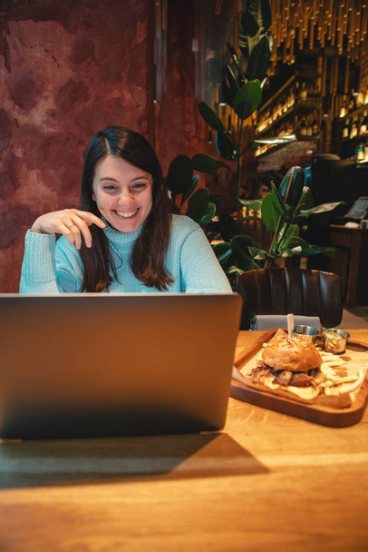 Kafede dizüstü bilgisayarda çalışan, çay içen, hamburger yiyen serbest çalışan bir kadın. - Fotoğraf, Görsel