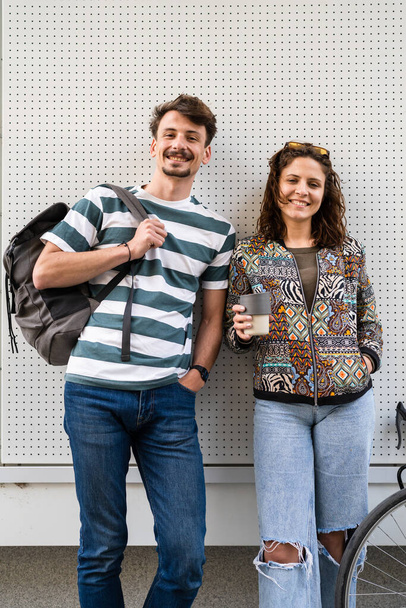 man and woman young couple posing in front of white wall of modern building in day students or tourists caucasian male with mustaches boyfriend and girlfriend happy smile looking to the camera - Photo, Image