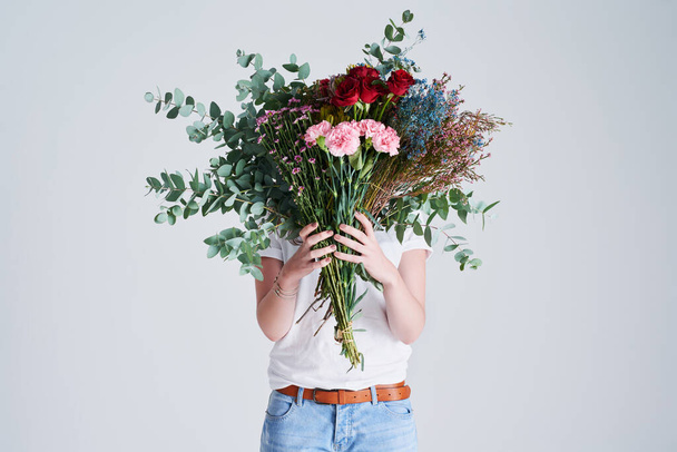 Sevdiğin biri için çiçekler. Gri bir arka planda yüzünü çiçeklerle kaplayan tanınmayan bir kadının stüdyo fotoğrafı.. - Fotoğraf, Görsel