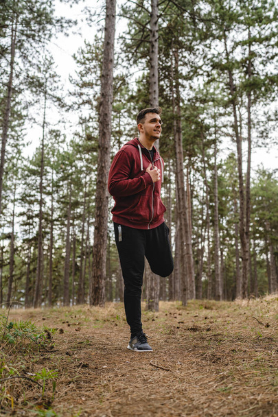 One man stretching in nature in forest or public park young adult caucasian male preparing for outdoor training in day standing alone real people copy space full length - Foto, Bild