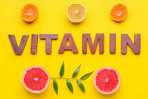 Text VITAMIN made of wooden letters and citrus fruits on yellow background - Fotografie, Obrázek