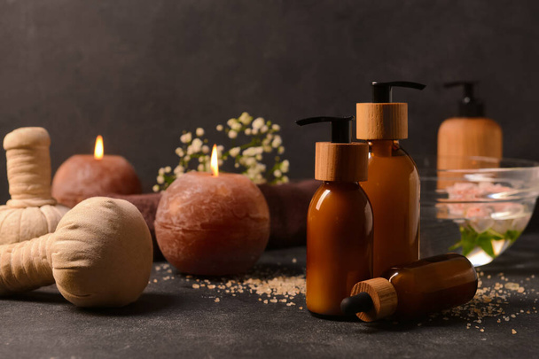 Bottles of cosmetic products, herbal bags and burning candles on dark background - Photo, Image