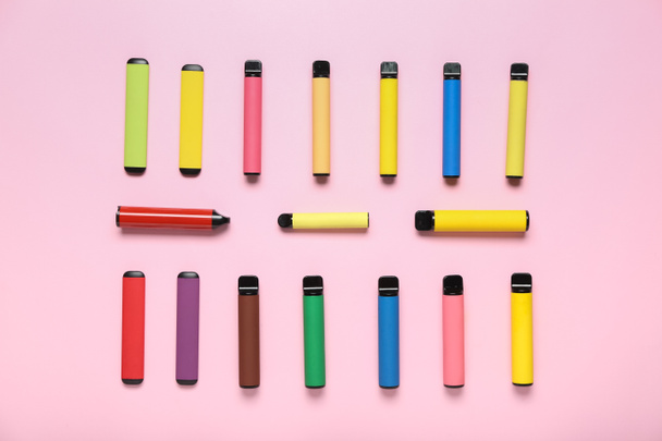 Different modern disposable electronic cigars on pink background - Photo, Image