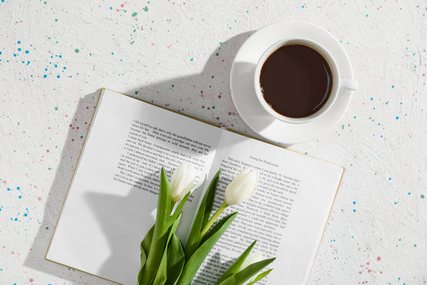 Opened book, cup of coffee and beautiful flowers on light background - Фото, изображение