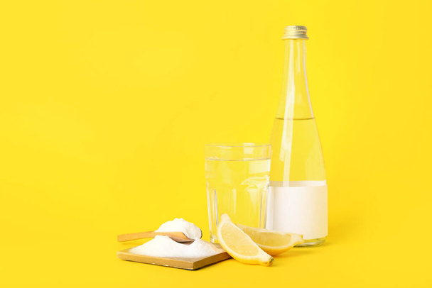 Σύνθεση με μαγειρική σόδα, ώριμο λεμόνι και νερό σε κίτρινο φόντο - Φωτογραφία, εικόνα