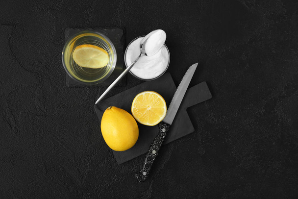 Bowl with baking soda, glass of water and lemons on dark background - Photo, image