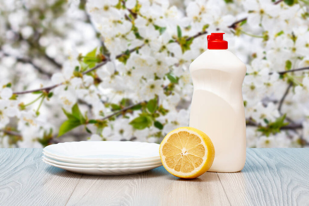 Bottle of dishwashing liquid, plates and lemon on natural background. - Foto, afbeelding