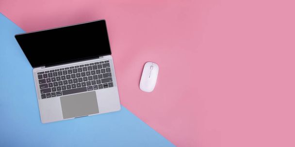 ピンクと青の背景にノートパソコンとワイヤレスマウス。コピースペース。トップビュー. - 写真・画像