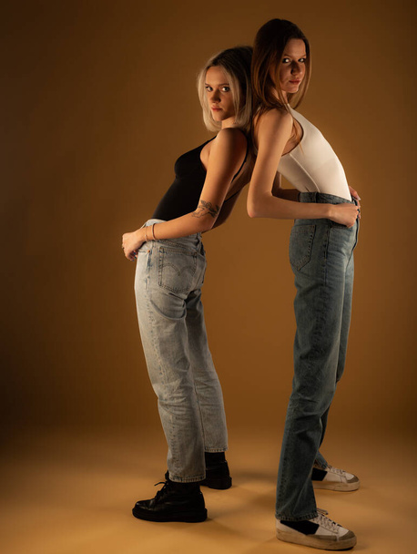 Two amazing and attractive girl friends are posing together in studio on yellow background while being dressed casual - Valokuva, kuva