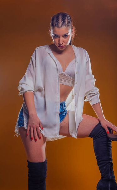 Молода жінка в стильному вбранні з білою лляною сорочкою і синіми короткими джинсами позує ізольовано в студії
 - Фото, зображення