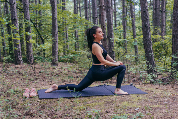 Zdrowa młoda, wysportowana kobieta robi sobie drzazgi na macie do jogi w lesie - Zdjęcie, obraz