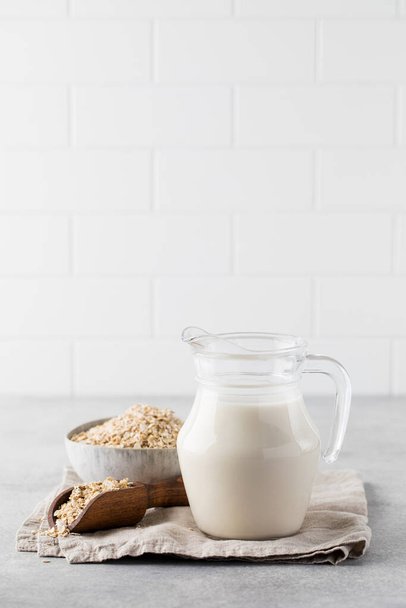 A jug of oat milk, a bowl of oatmeal on the table on a light background. Copy space. - Foto, Bild