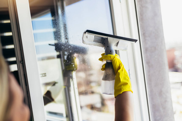 Glückliche Schöne Frau mit Schutzhandschuhen Fensterputzen durch Sprühen von Reinigungsprodukten und Wischen mit Schwamm. - Foto, Bild