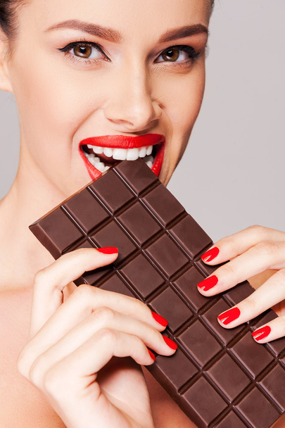 Beautiful woman with red lips biting chocolate bar - Fotoğraf, Görsel