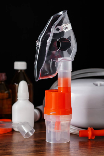 Atemmaske für Kompressorvernebler mit verschiedenen medizinischen Geräten zur Inhalationstherapie bei Asthma und Atemwegserkrankungen auf dem Tisch, selektiver Fokus. - Foto, Bild