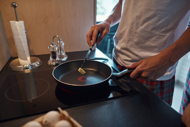 Man put butter with knife on pan on electric stove - Zdjęcie, obraz