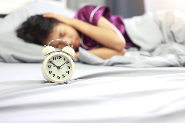 Wake up concept - Asian girl covering her ear with hand from alarm clock noise in her bedroom in the morning. Upset asian girl being awaken with alarm clock. - Photo, Image