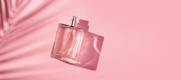 Transparent bottle of perfume on a pink background. Fragrance presentation with daylight. Trending concept in natural materials palm leaves shadow. Women's and men's essence. - Фото, изображение