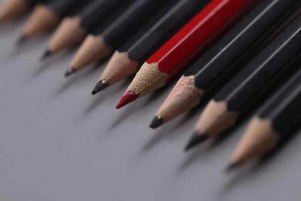 One red pencil between row of black pencils - 写真・画像