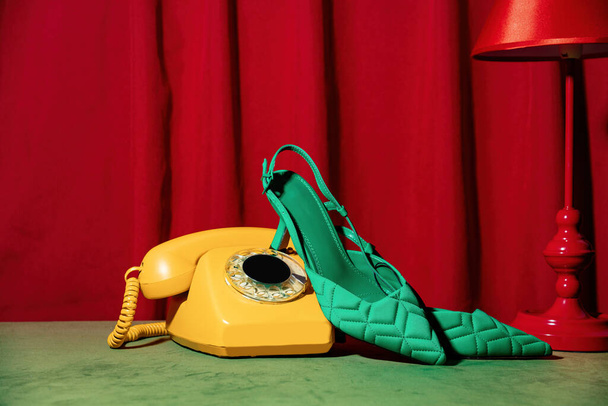 Vitnage teléfono y tacones verdes en una mesa junto a la lámpara roja y cortinas - Foto, Imagen
