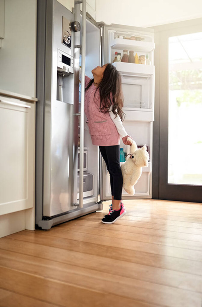 Auf der Suche nach einem Imbiss. Aufnahme eines kleinen Mädchens, das zu Hause nach etwas im Kühlschrank greift. - Foto, Bild