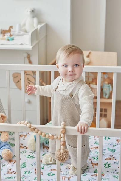 Wonderful baby boy with blue eyes in crib. Child playing with toys in nursery. Early development, kindergarten, nursery, playroom. Children's Day, Mother's Day. - Fotó, kép