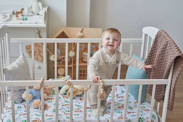 Wonderful baby boy with blue eyes in crib. Child playing with toys in nursery. Early development, kindergarten, nursery, playroom. Children's Day, Mother's Day. - 写真・画像