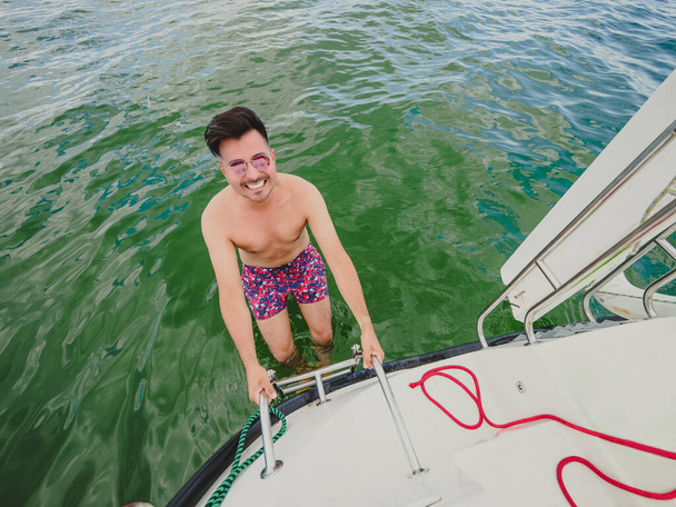 Happy black hair man down the ladder into the water. A man down into the water on an iron ladder on the sailing yacht a to swim - Zdjęcie, obraz